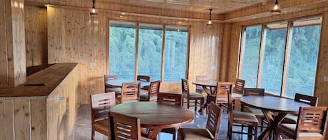 Un interior de madera con una zona de bar, varias mesas de comedor y ventanas amplias.