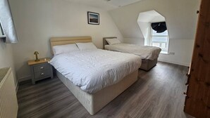 Ein Schlafzimmer mit zwei Betten, einem Nachttisch, einer Lampe und einem Fenster mit Aussicht.