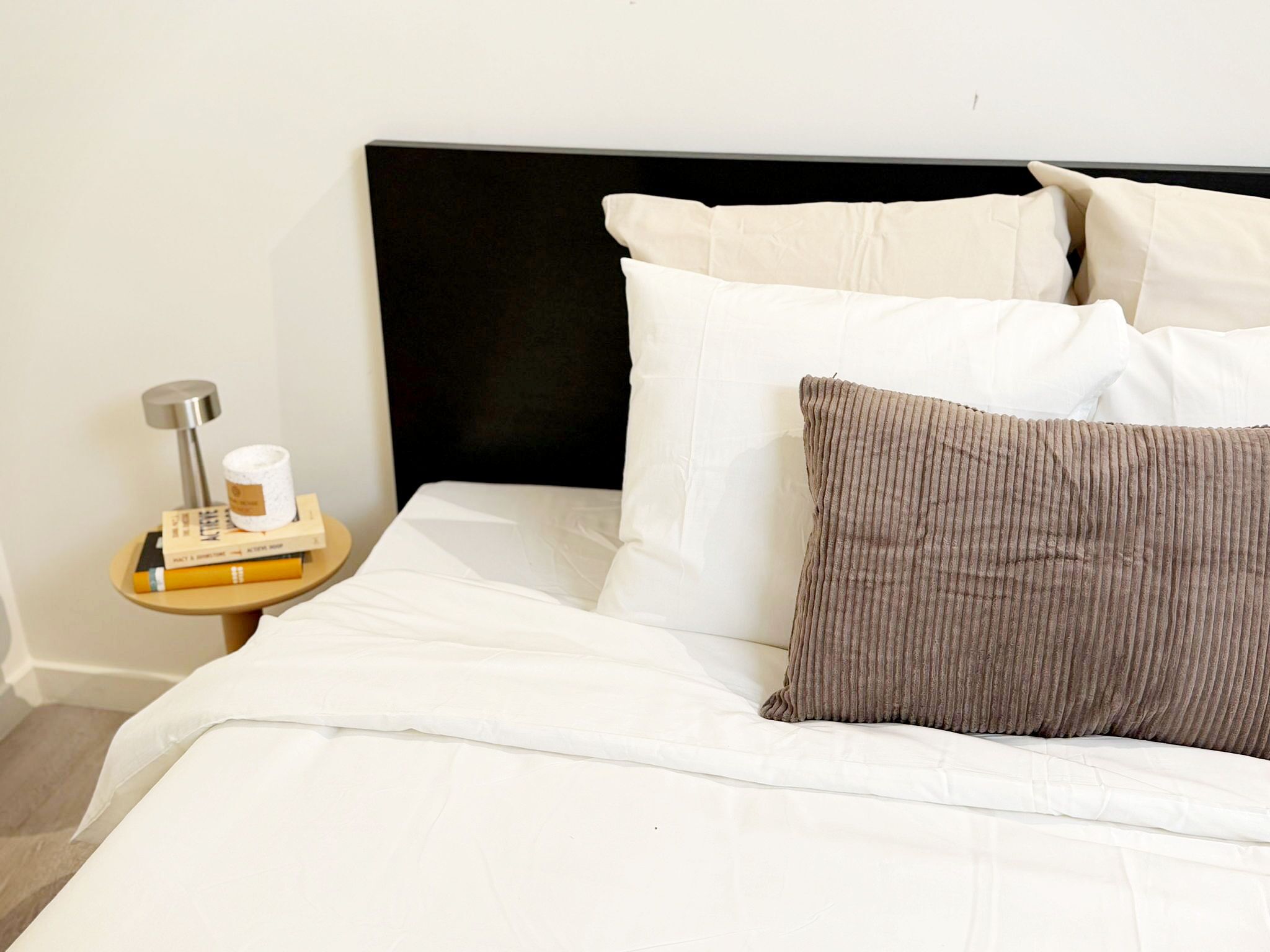 A neatly made bed with white linens, a black headboard, and a brown pillow.