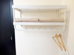 Una repisa blanca con una toalla beige enrollada y perchas de madera.