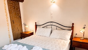 A neatly made bed with white linens and a blue quilt, two bedside tables with lamps, a wooden headboard, and a decorative wall panel. - Hidden Oasis Amazing Seaview - Erato 1BD 1BA 4PL (Apokoronas)