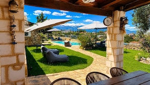 A patio with stone walls, a pool, outdoor seating, and a view of a mountain range. - Hidden Oasis Amazing Seaview - Erato 1BD 1BA 4PL (Apokoronas)