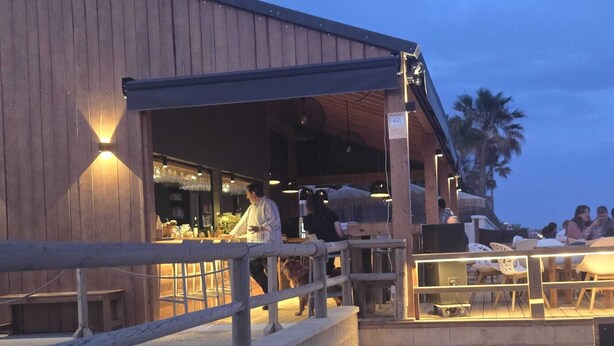 Een restaurant met terras, een houten gevel en een persoon die bij de ingang staat.