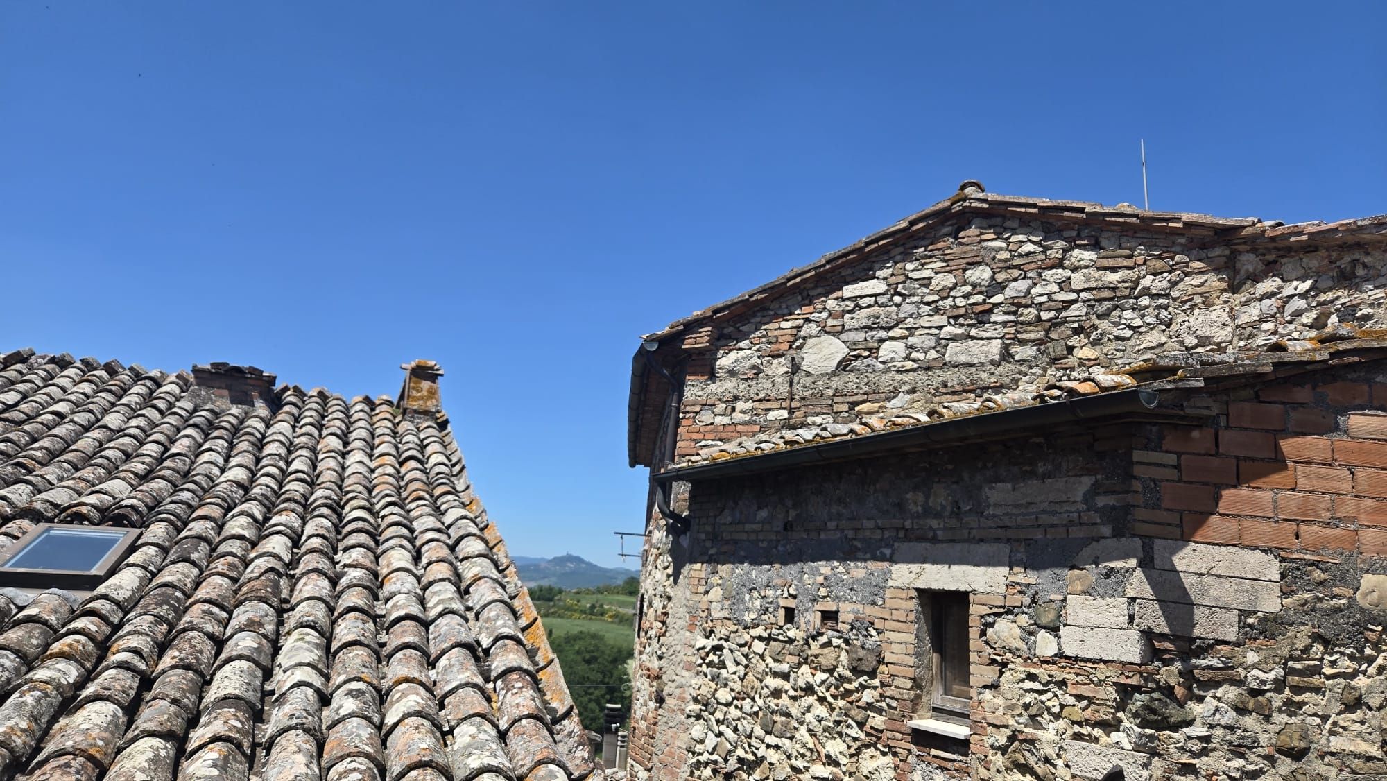 A traditional stone building with a tiled roof, a small window, and a chimney.