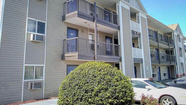 A multi-story apartment building with balconies, air conditioning units, and a well-maintained hedge. - 2 Queen Beds|Suite|Smk|Kitchen (Fayetteville)
