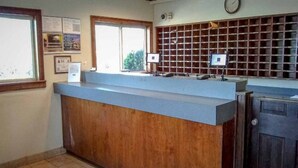 A reception desk with a wooden counter, a window, a wall-mounted clock, and a bulletin board.