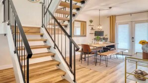 A staircase with wooden steps and black railings, a dining area with a table and chairs, and a large window with curtains. - Awesome 4-bedroom townhome with AC in sunny Scottsdale (Scottsdale)