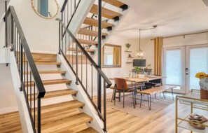 Eine Treppe mit Holzstufen und schwarzen Geländern, ein Essbereich mit Tisch und Stühlen sowie ein großes Fenster mit Vorhängen.