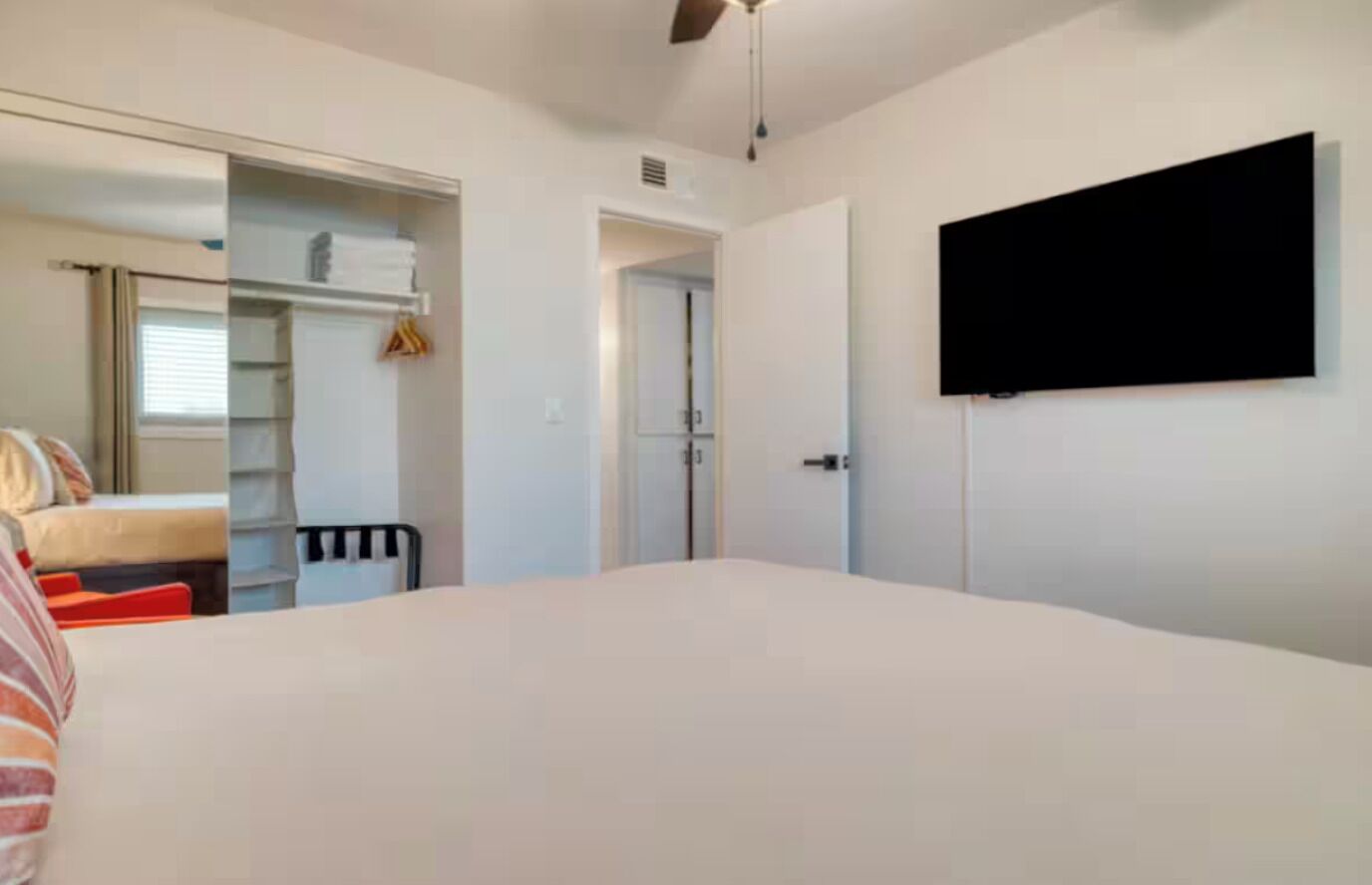 Une chambre à coucher avec un lit, une armoire, un miroir et un téléviseur fixé au mur.