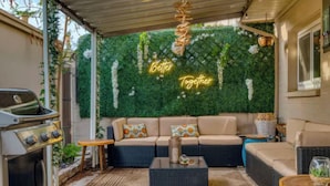 An outdoor patio with a grill, a sofa set, and a wall with greenery and a neon sign. - Awesome 4-bedroom townhome with AC in sunny Scottsdale (Scottsdale)