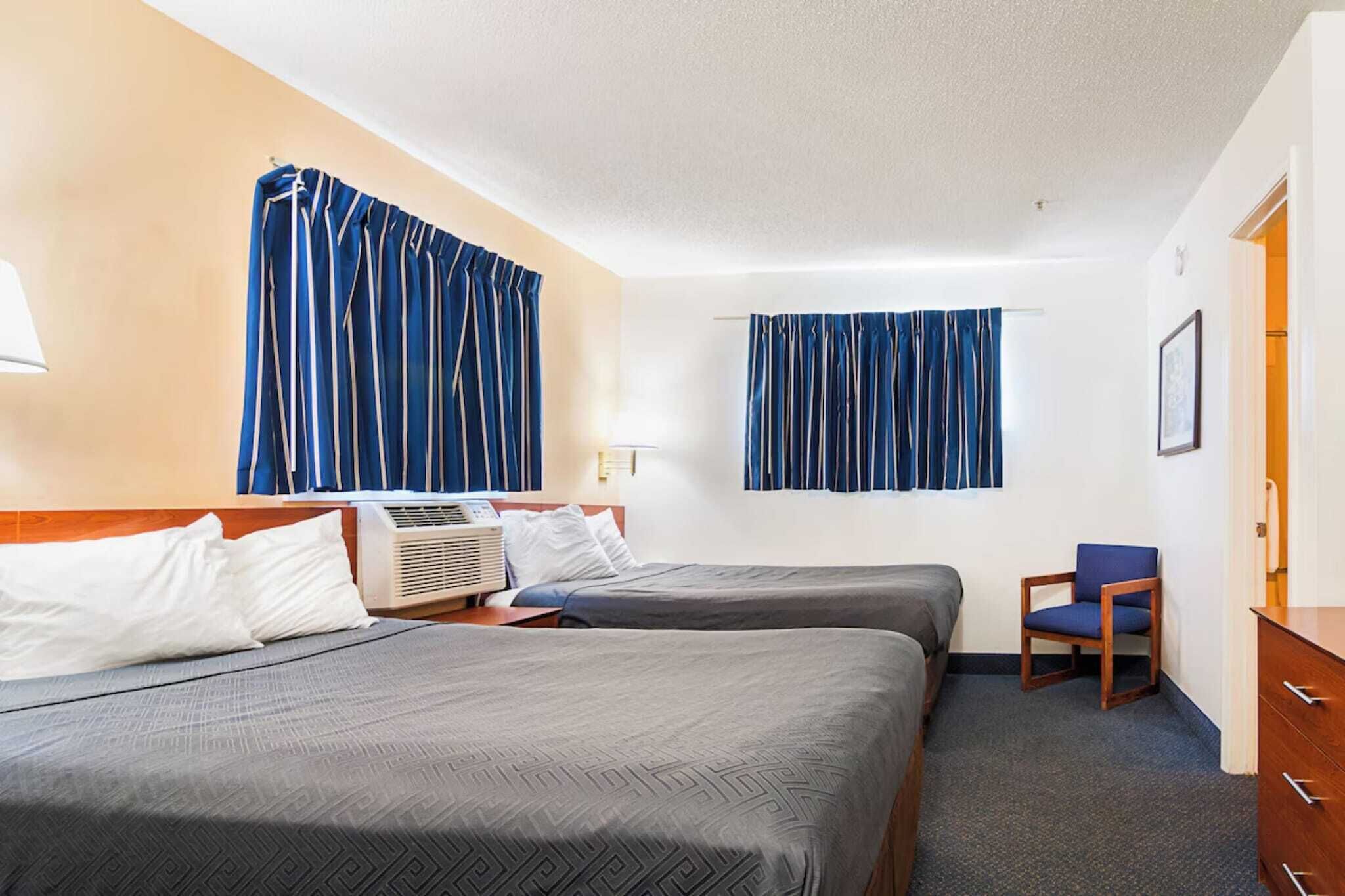 A hotel room with two beds, a chair, a dresser, and a window with curtains.