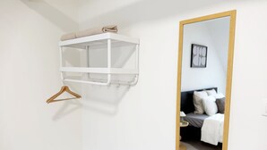 Una habitación blanca con una cama, un espejo de marco de madera y un estante blanco con una toalla.