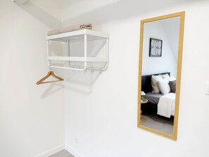 Ein heller Raum mit einem Bett, einem Spiegel mit Holzrahmen und einem weißen Regal mit einem Handtuch.