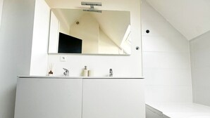 Un baño moderno con un espejo grande, un tocador blanco y una bañera.