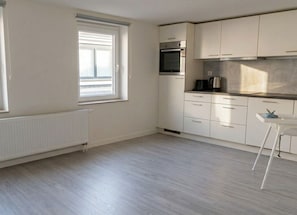 Een keuken met witte kastjes, een inbouwoven en een raam.