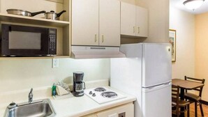 Una cucina compatta con forno a microonde, fornello, lavello e mobili bianchi.