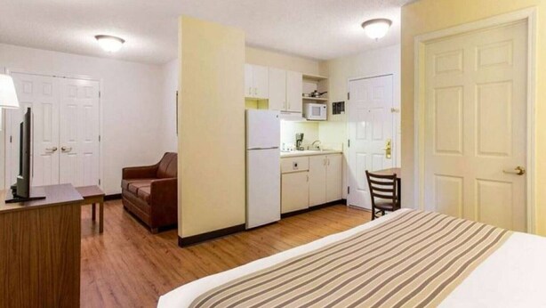 Camera d'albergo compatta con un letto, una scrivania, un divano, angolo cottura e una porta.