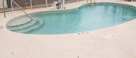 A swimming pool with a 3 FT depth marking, a lifeguard stand, and a fenced area with lounge chairs.