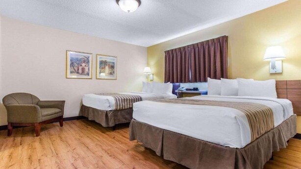 Quarto de hotel com duas camas, uma cadeira, uma escrivaninha e duas quadros na parede.