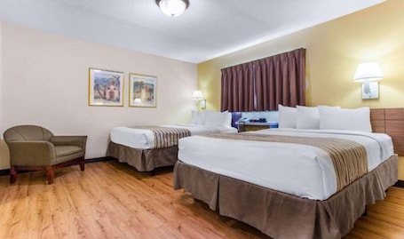 A hotel room with two beds, a chair, a desk, and two framed pictures on the wall.