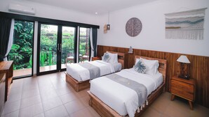 Ein Doppelzimmer mit zwei Betten, einem Holz-Kopfteil, einem Nachttisch, einem Schreibtisch und einem Balkon mit Blick auf Grünflächen.