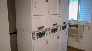 A laundry room with stacked dryers, a window, and a wall-mounted air conditioner.