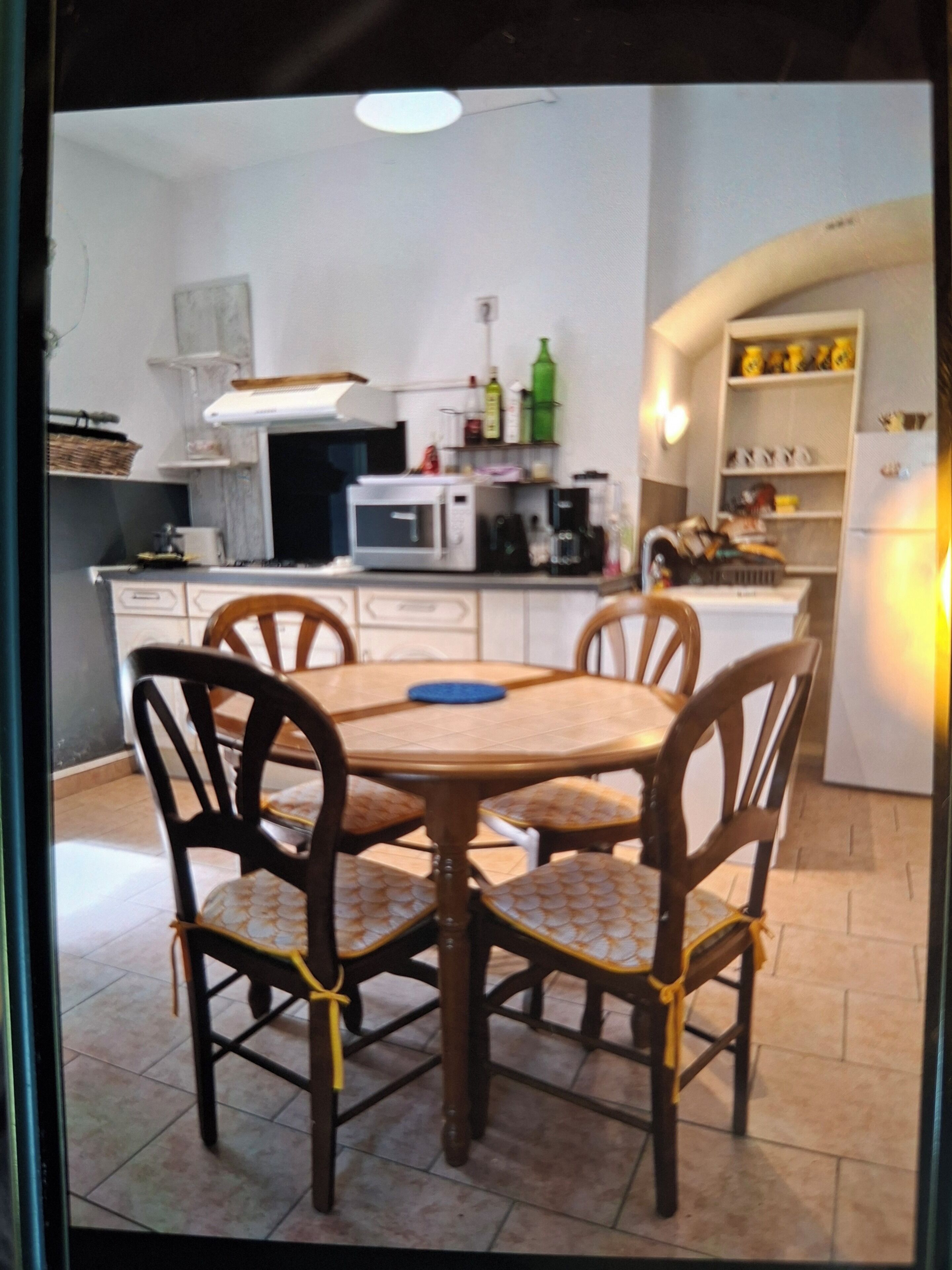 Ett kök med ett matbord och stolar, en mikrovågsugn, ett kylskåp och diverse köksredskap.