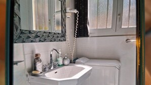 A compact bathroom with a white sink, a mirror, a towel rack, and a window with curtains. - House in the Cevennes (Molières-sur-Cèze)