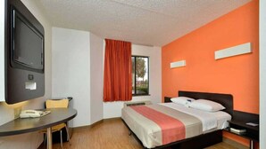 Ein Hotelzimmer mit Bett, Schreibtisch, Sessel, Fernseher und einem Fenster mit Vorhängen.