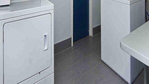 A laundry area with two white washing machines, a blue door, and a grey tiled floor.