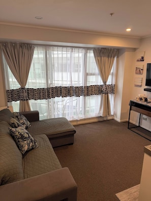 Ein Wohnzimmer mit einer Couch, einem Hocker und einem Tisch mit Fernseher.