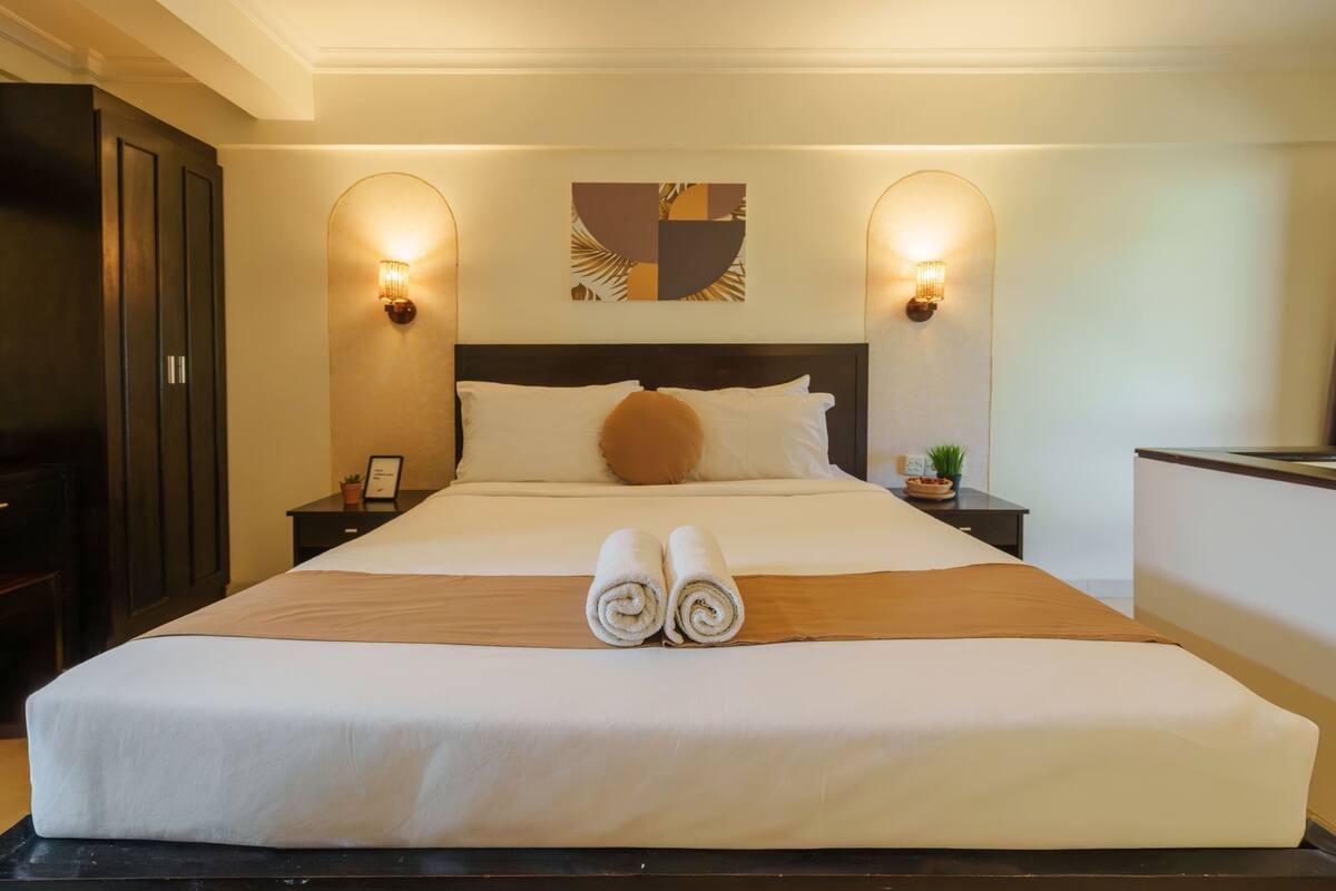 Quarto de hotel com uma cama grande, duas mesas de cabeceira, uma cabeceira e iluminação embutida na parede.