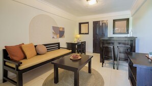A living area with a sofa, a coffee table, a small kitchen area with a bar stool, and a mirror. - Cove Premisol (Denpasar)