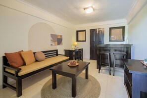 Sala de estar con sofá, una mesa de centro, una pequeña cocina con taburete de bar y un espejo.