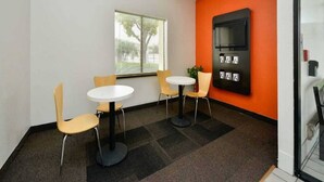 Une pièce comprenant deux tables rondes et quatre chaises, une grande fenêtre et un téléviseur fixé au mur.
