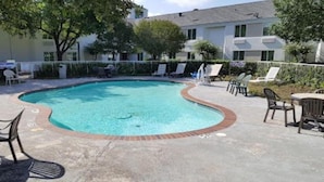 A swimming pool with lounge chairs and tables, surrounded by a fence and trees.