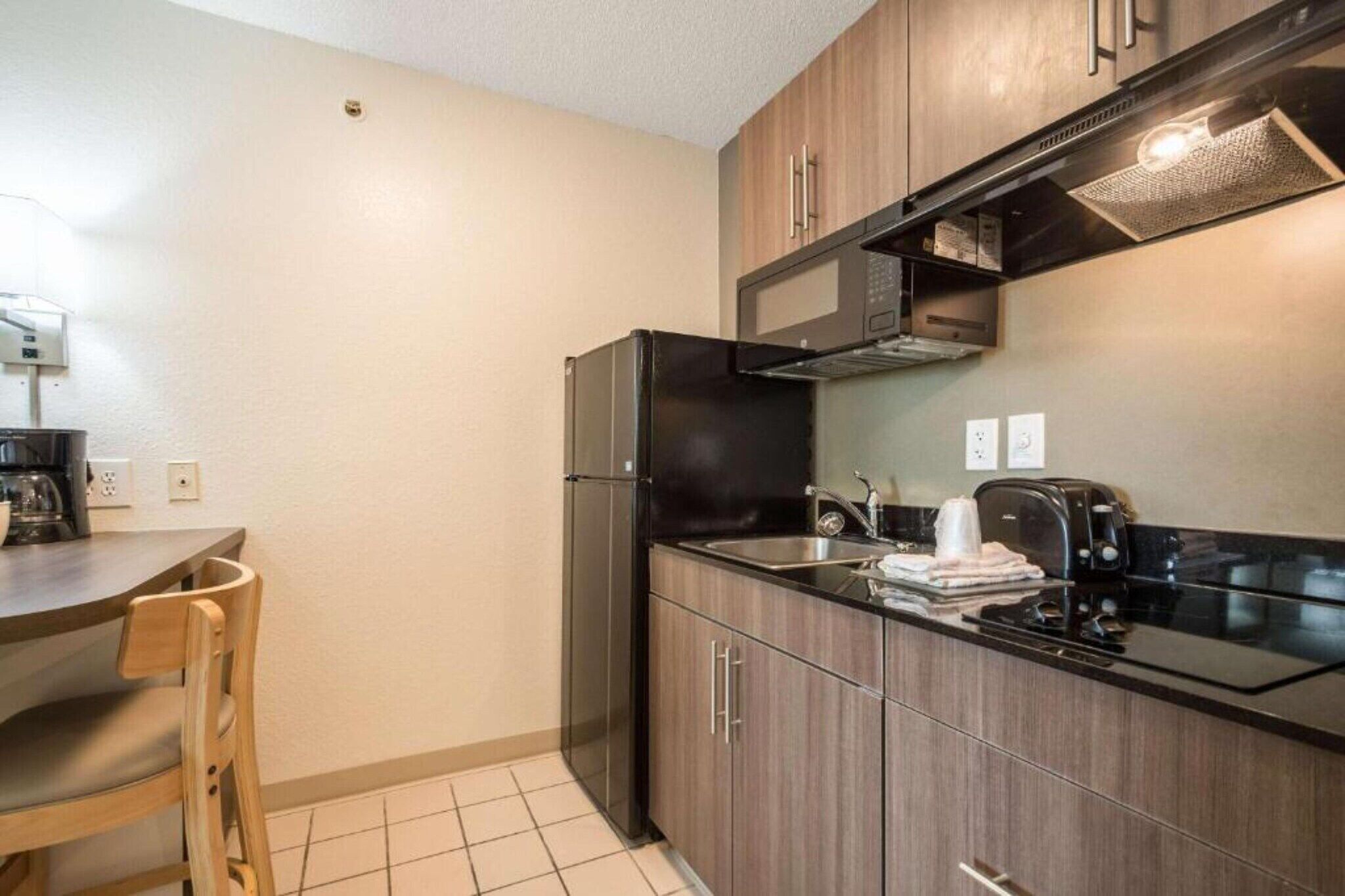 A compact kitchen with a refrigerator, microwave, stove, and a small dining area with a chair.