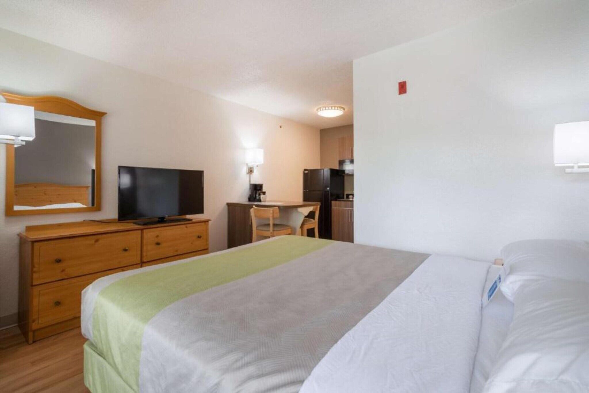 Een hotelkamer met een bed, een bureau, een stoel, een televisie en een spiegel.