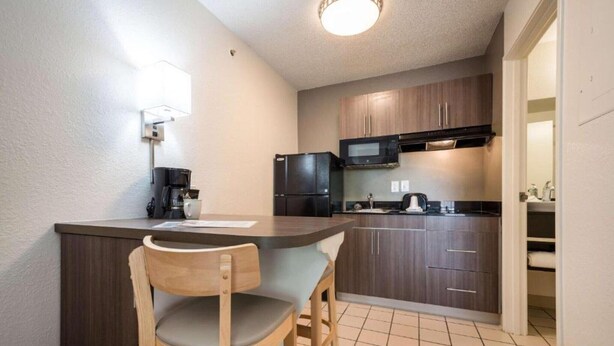 A compact kitchen with a wooden bar counter, a microwave, a refrigerator, and a sink.