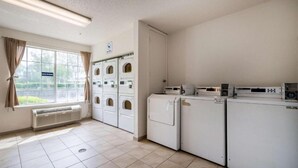 A laundry facility with multiple washing machines and dryers, a window with curtains, and a sign indicating the facility is for guests.