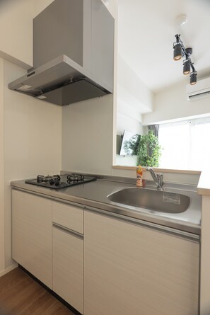 A kitchen with a gas stove, stainless steel sink, and a modern range hood. - Premiage Minoshima (Hakata Ward, Fukuoka)