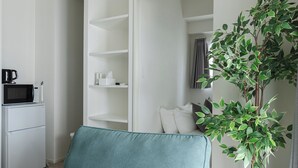 Une chambre moderne avec un lit, une armoire blanche, un petit coin cuisine et une plante en pot.