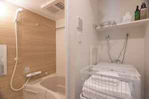 A bathroom with a bathtub, a shower, a towel rack, and a shelf with toiletries. - Premiage Minoshima (Hakata Ward, Fukuoka)