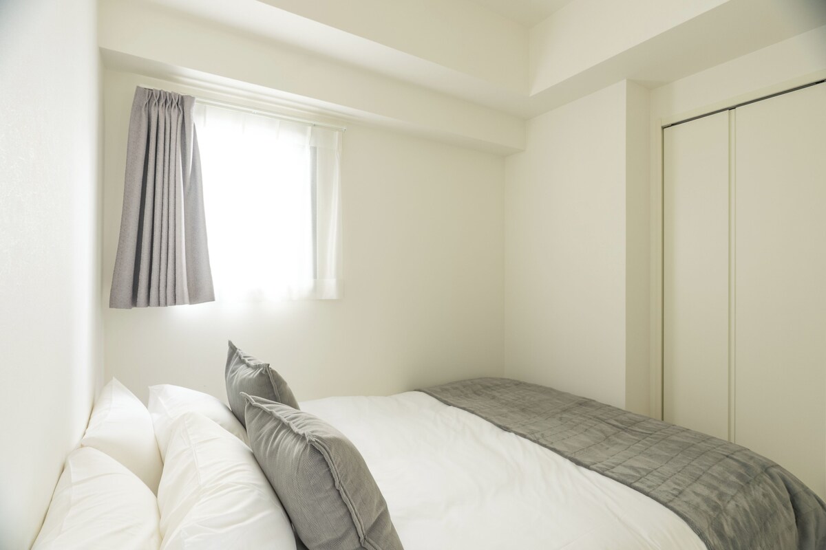 A bedroom with a bed, a window with curtains, a wardrobe, and a bedside table.