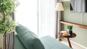 Un salon moderne avec un canapé vert, une plante en pot, une petite table avec une lampe et un téléviseur à écran plat fixé au mur.