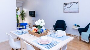Un comedor con una mesa dispuesta para dos personas, una cesta de fruta y un jarrón de flores.