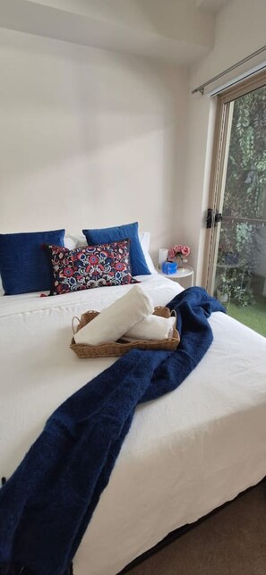 A bed with white bedding, blue pillows, and a blue blanket. There is a wicker basket with folded towels and a small table with a vase of flowers. - City central hideway GLEBE  + Free Parking (Glebe)