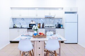 A modern kitchen with white cabinets, a marble backsplash, and a dining area with two white chairs and a table set for two. - City central hideway GLEBE  + Free Parking (Glebe)