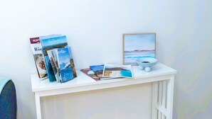 Una consola blanca con folletos de viaje, un cuadro enmarco y un tazón blanco.