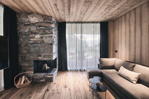 A cozy living room with a stone fireplace, wooden flooring, a sofa, and a TV. - Luxurious Chalet in the Racines forest with private jacuzzi (Racines)